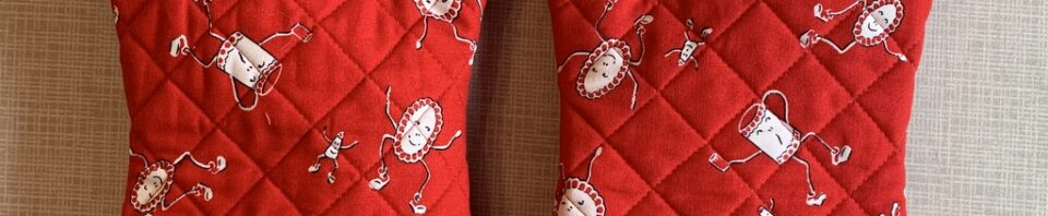 Red oven mitts with whimsical printed designs.