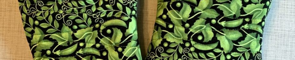 Green floral-patterned oven mitts on table.