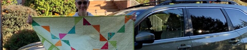 Woman holding colorful quilt near car.