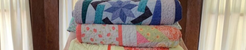 Woman holding colorful stacked quilts indoors.