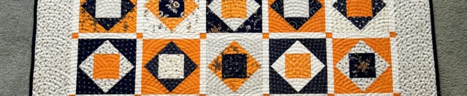 Quilt featuring orange, black, and white patterns.